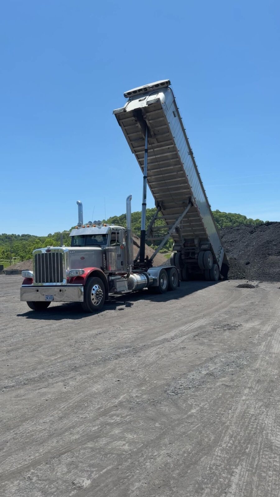 Titan Trucking end dump raised, unloading aggregate under a blue sky