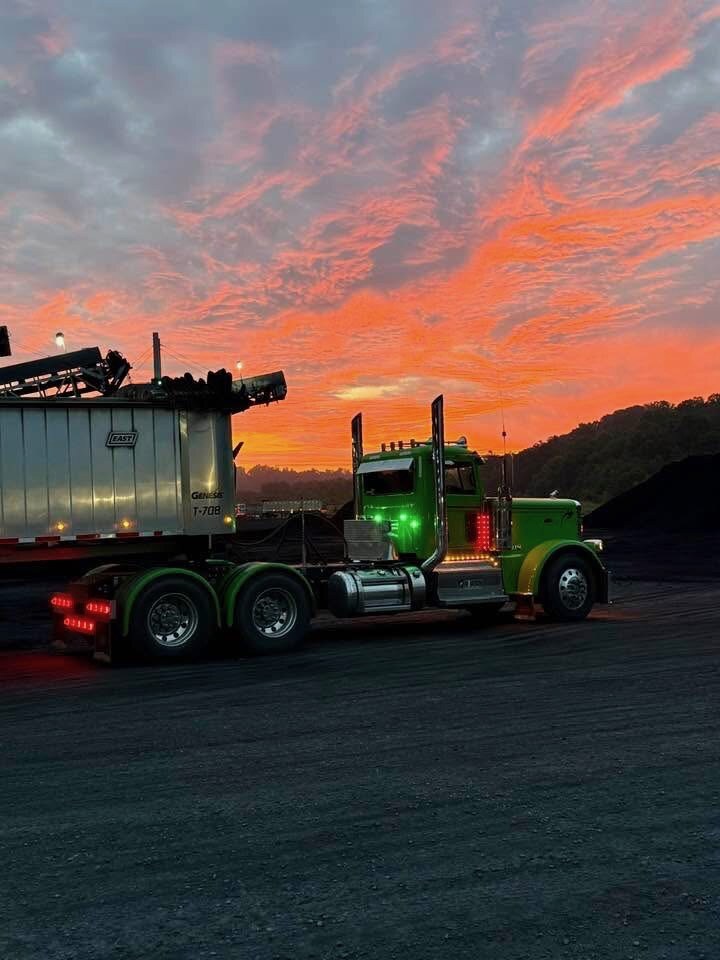 Lime green Titan Trucking Peterbilt with end dump under a fiery sunset