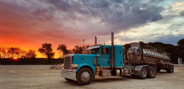 Turquoise Titan Peterbilt with vacuum trailer under a red sunset
